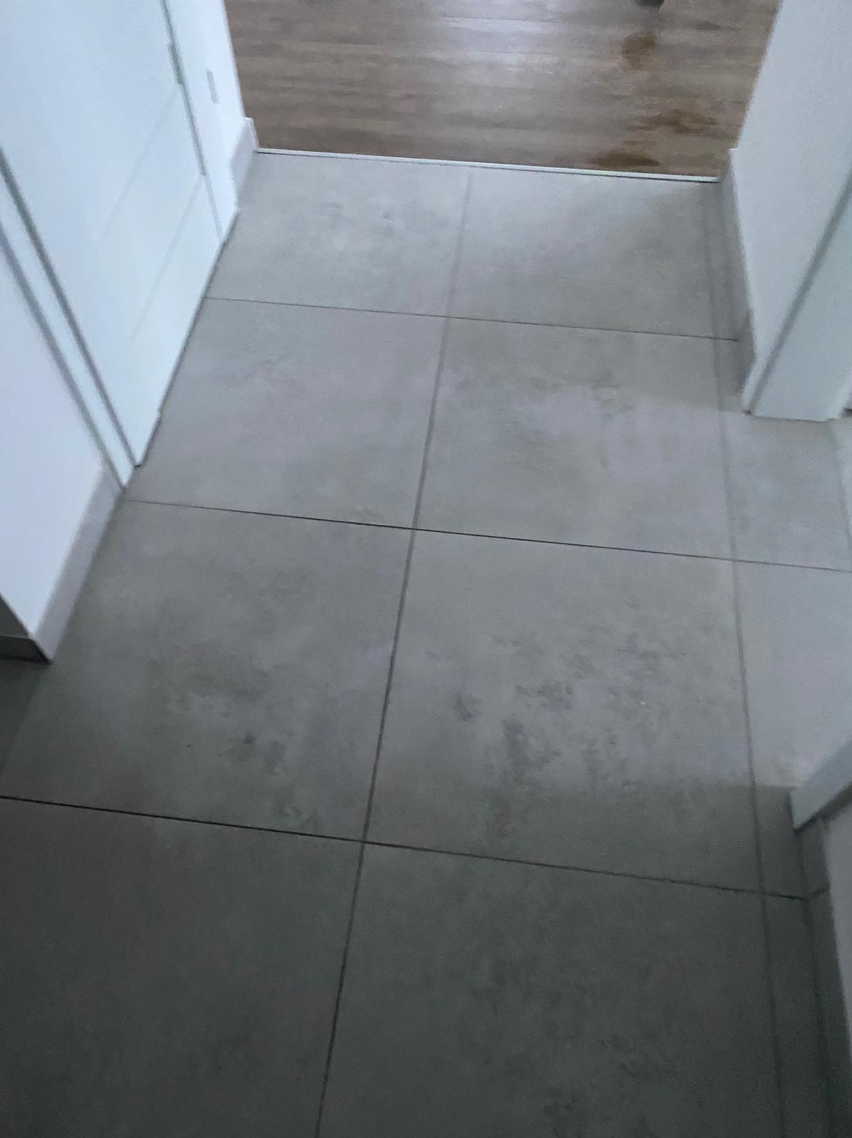 Ułożone szare płytki podłogowe w przedpokoju, widoczne fragmenty białych drzwi i drewnianej podłogi. Minimalistyczne wykończenie wnętrza.