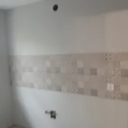 Świeżo położone, beżowe płytki dekoracyjne na ścianie w pustym pomieszczeniu, widoczne puszki elektryczne w ścianie i suficie, przygotowane do dalszych prac.