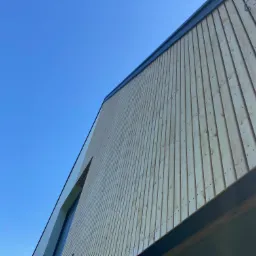 Nowoczesny dom z elewacją z jasnego drewna, pionowe deski, widok z dołu pod kątem, błękitne niebo w tle.