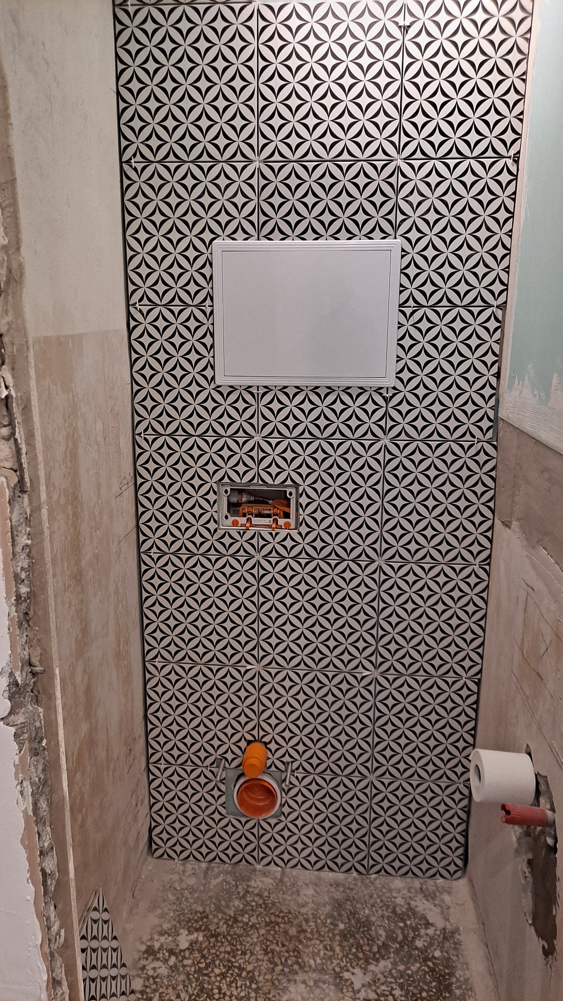 Montaż czarno-białych płytek z geometrycznym wzorem w toalecie, widoczna instalacja podtynkowa i fragment ściany z resztkami zaprawy.