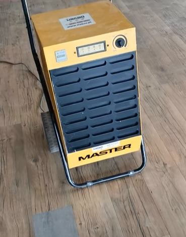 Żółty, przemysłowy osuszacz powietrza marki Master na drewnianej podłodze, widoczny panel sterowania z wyświetlaczem i pokrętłem.