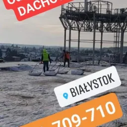 Dwóch pracowników z łopatami usuwa śnieg z dachu konstrukcji w Białymstoku, widoczny numer telefonu kontaktowego.