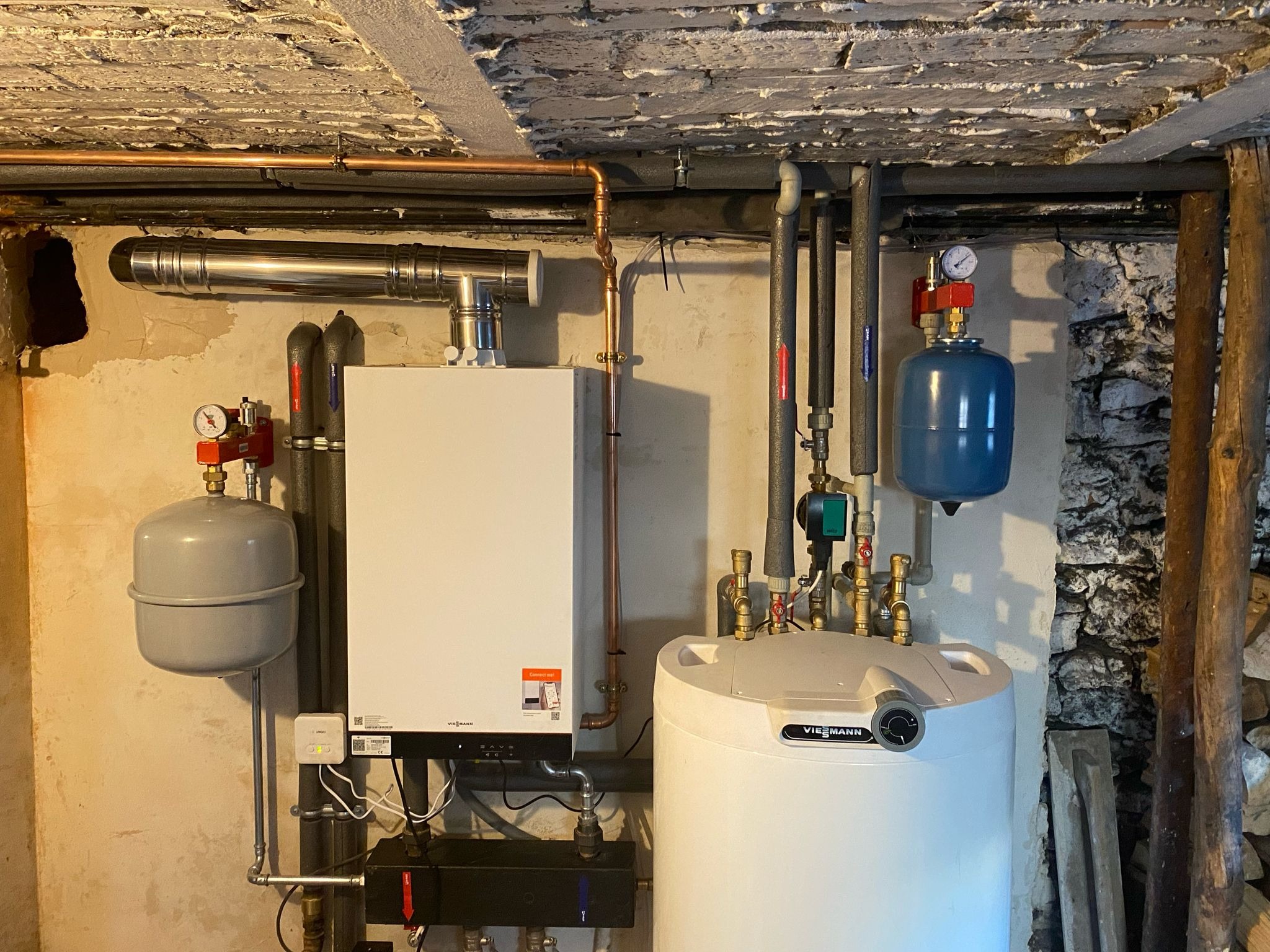 Zestaw urządzeń grzewczych Viessmann: piec i zasobnik ciepłej wody z osprzętem, zainstalowane w piwnicy o surowym, ceglanym wykończeniu.