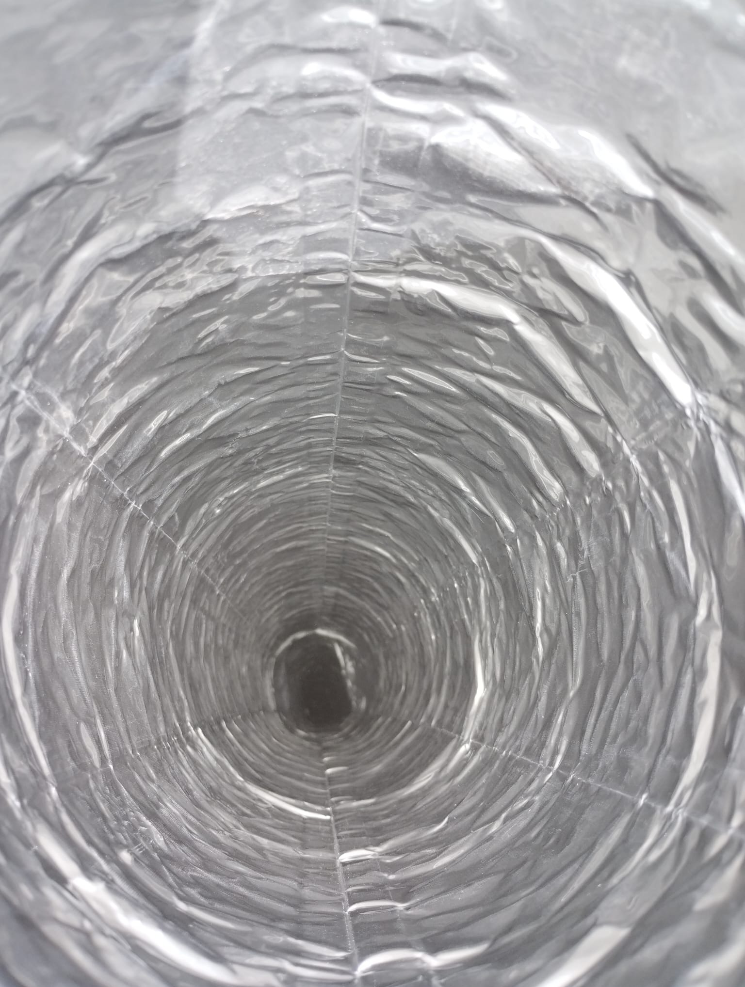 Wnętrze elastycznego, aluminiowego przewodu wentylacyjnego, widok z perspektywy, z delikatnymi załamaniami i spiralnym wzorem.
