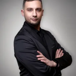 Portret mężczyzny w czarnym garniturze, skrzyżowane ręce, patrzący wprost, na szarym tle.