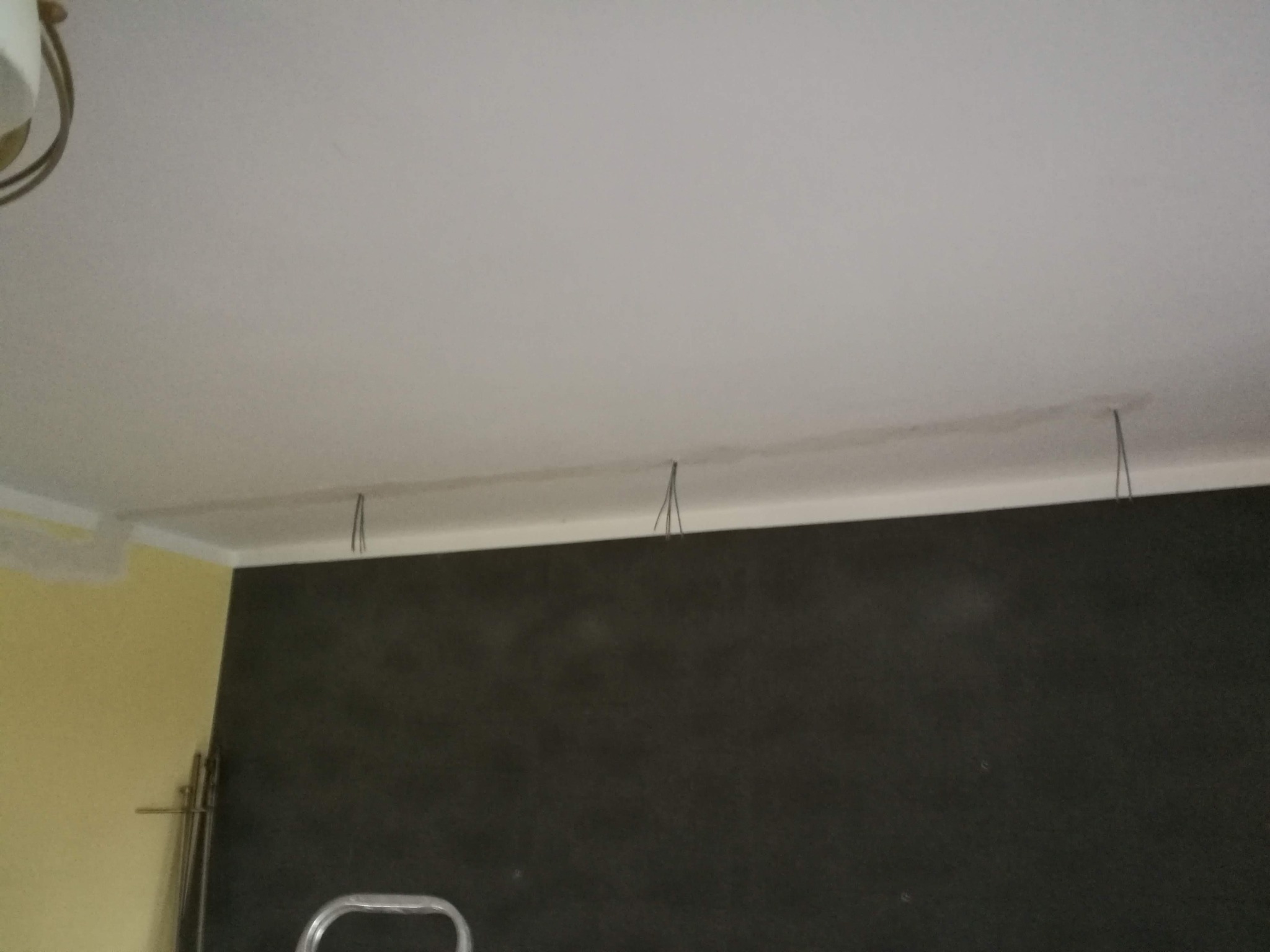 Przygotowanie do montażu oświetlenia: wiszące przewody elektryczne z sufitu, widoczny fragment drabiny i pomalowana ściana w tle.