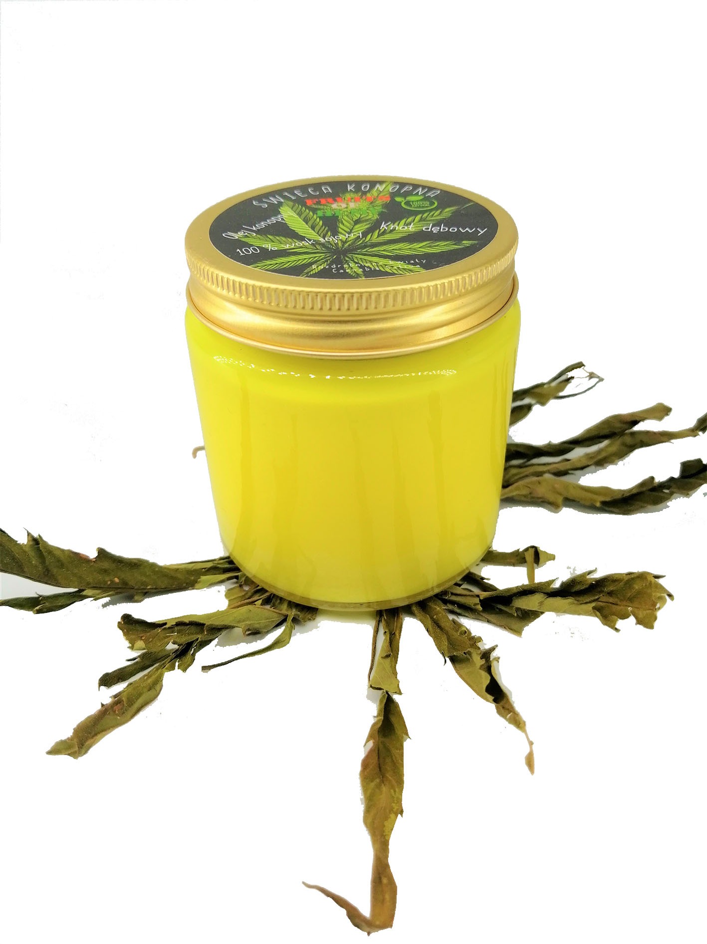 Żółta świeca konopna w słoiczku z etykietą, otoczona suszonymi liśćmi na białym tle.