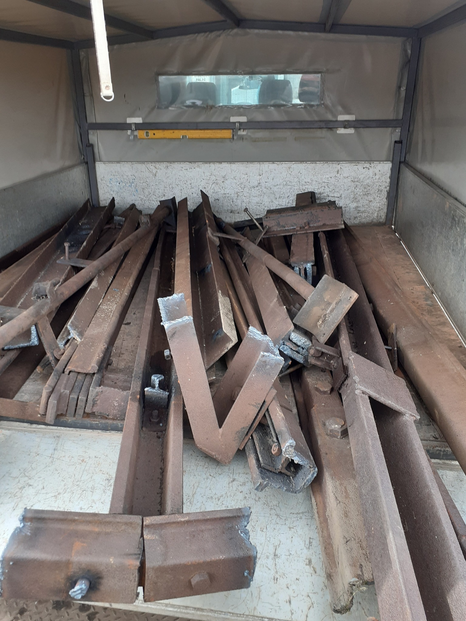 Stalowe, zardzewiałe elementy konstrukcyjne, prawdopodobnie pozostałości po rozbiórce, ułożone w skrzyni transportowej. Widoczne ślady cięcia i spawania.