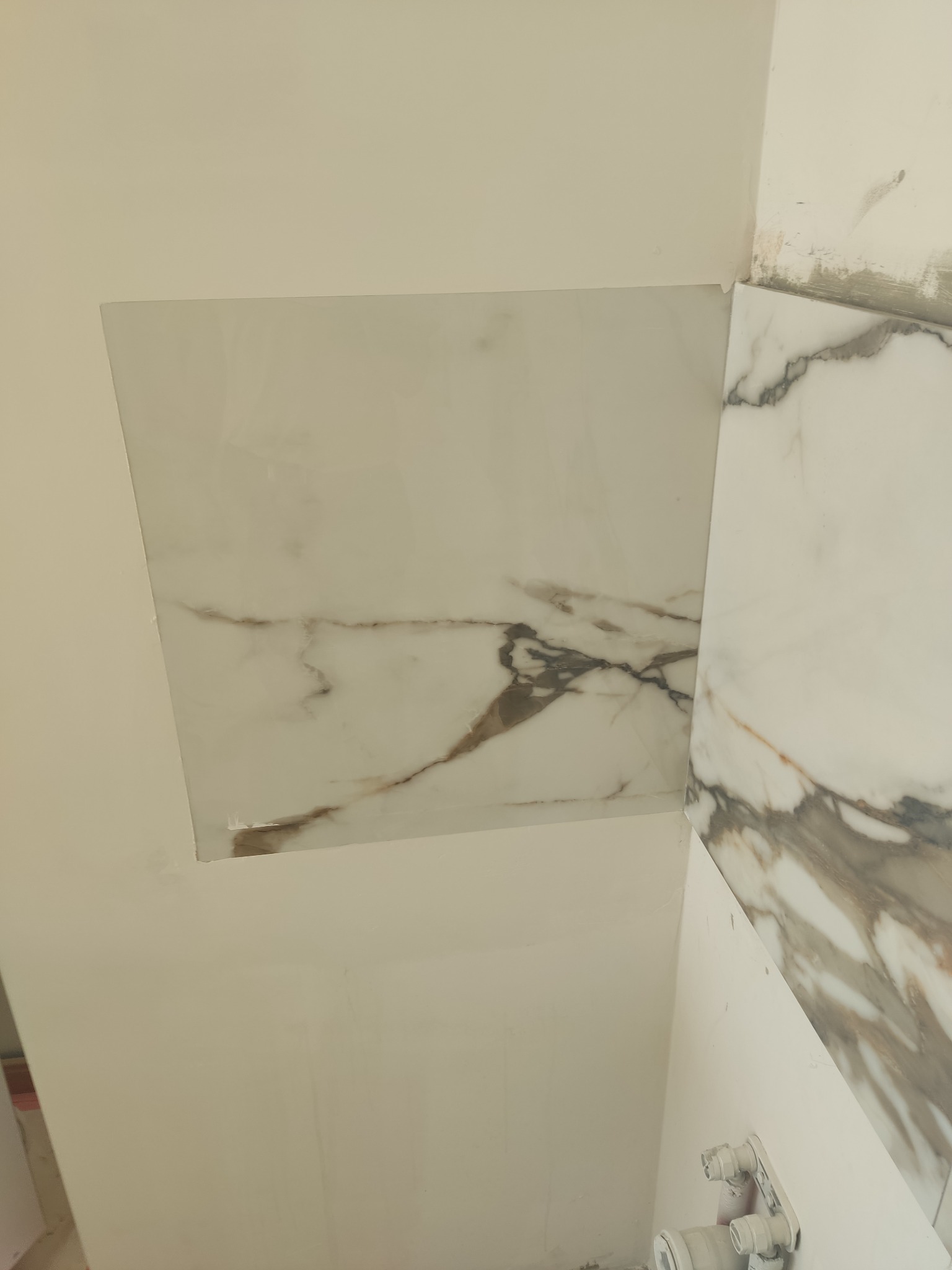 Fragment ściany z ułożonymi płytkami imitującymi marmur, widoczne niedociągnięcia w fugach i ślady zaprawy.