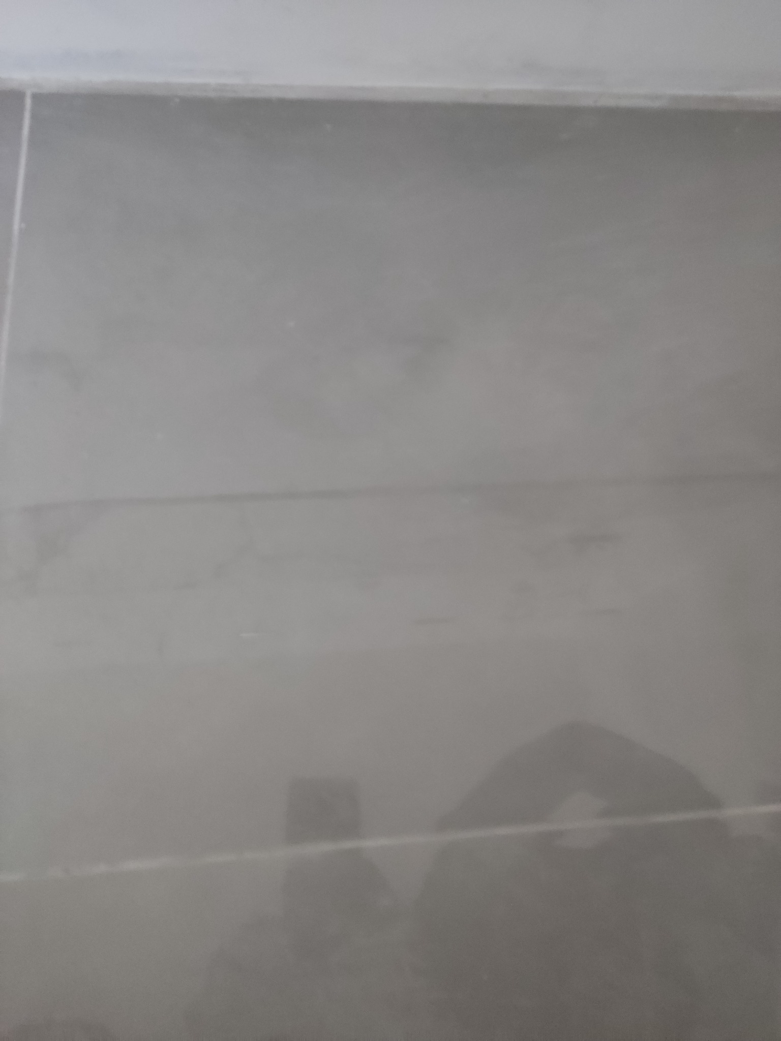 Szare, błyszczące płytki ceramiczne ułożone na podłodze, widoczne fugi i odbicie fotografa w powierzchni płytek.