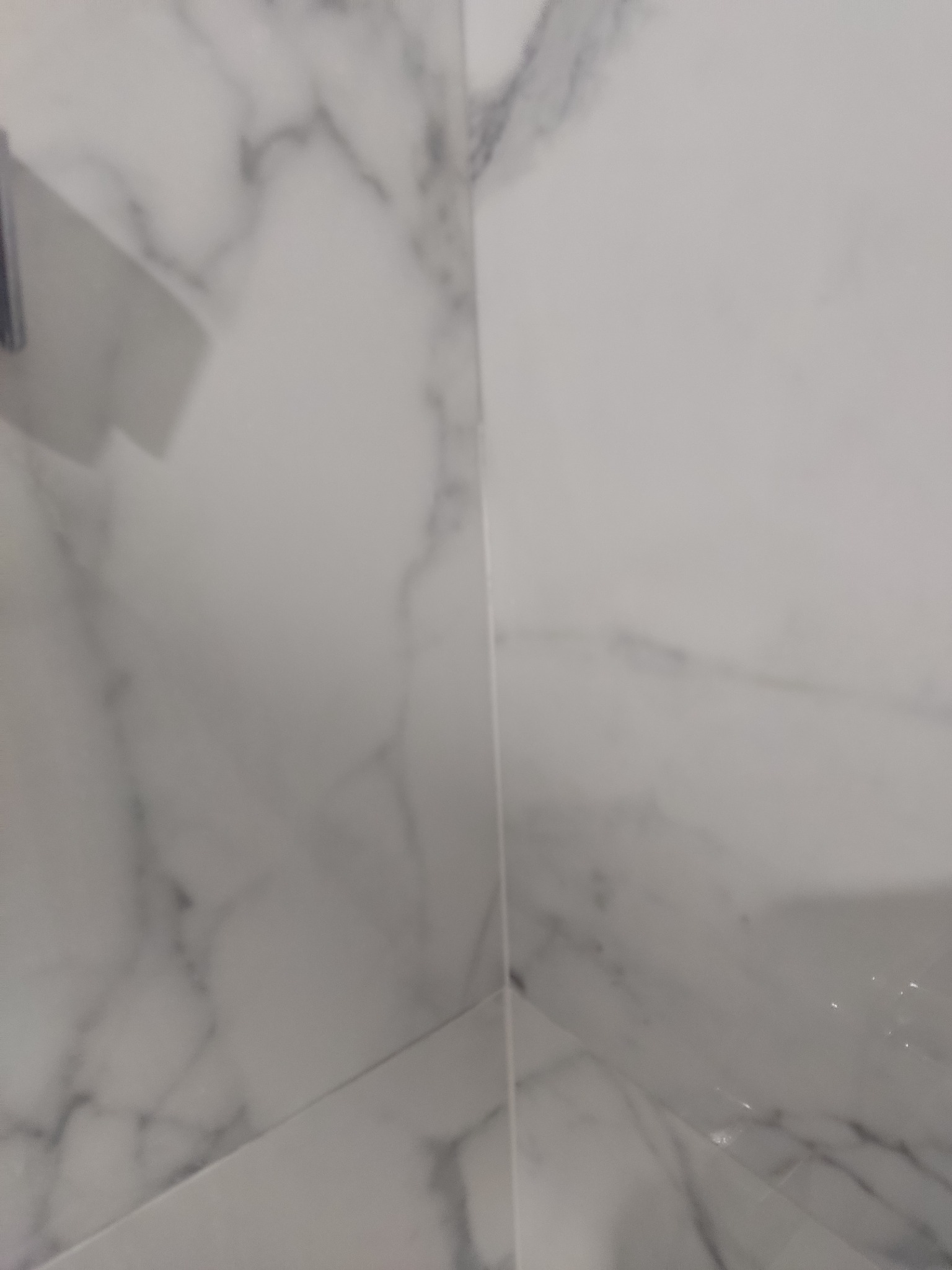 Białe płytki imitujące marmur ułożone na ścianie w rogu pomieszczenia, widoczne fugi.