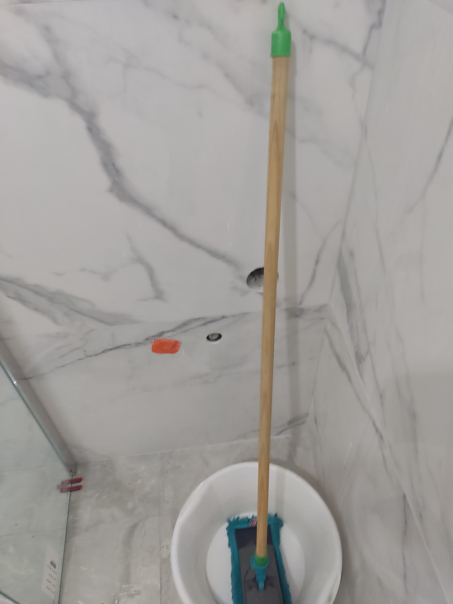 Mop w wiadrze stoi w łazience z marmurowymi płytkami na ścianach, widoczne otwory na oświetlenie.