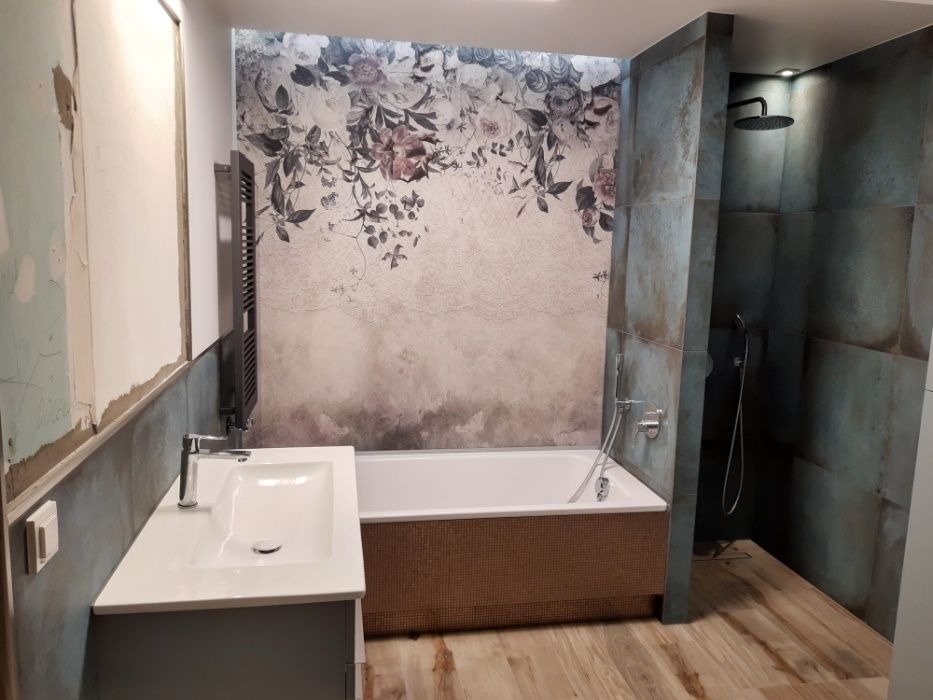 Nowoczesna łazienka z motywem kwiatowym na ścianie, kabina prysznicowa w odcieniach szarości, drewnopodobne panele na podłodze i fragment ściany w trakcie prac wykończeniowych.