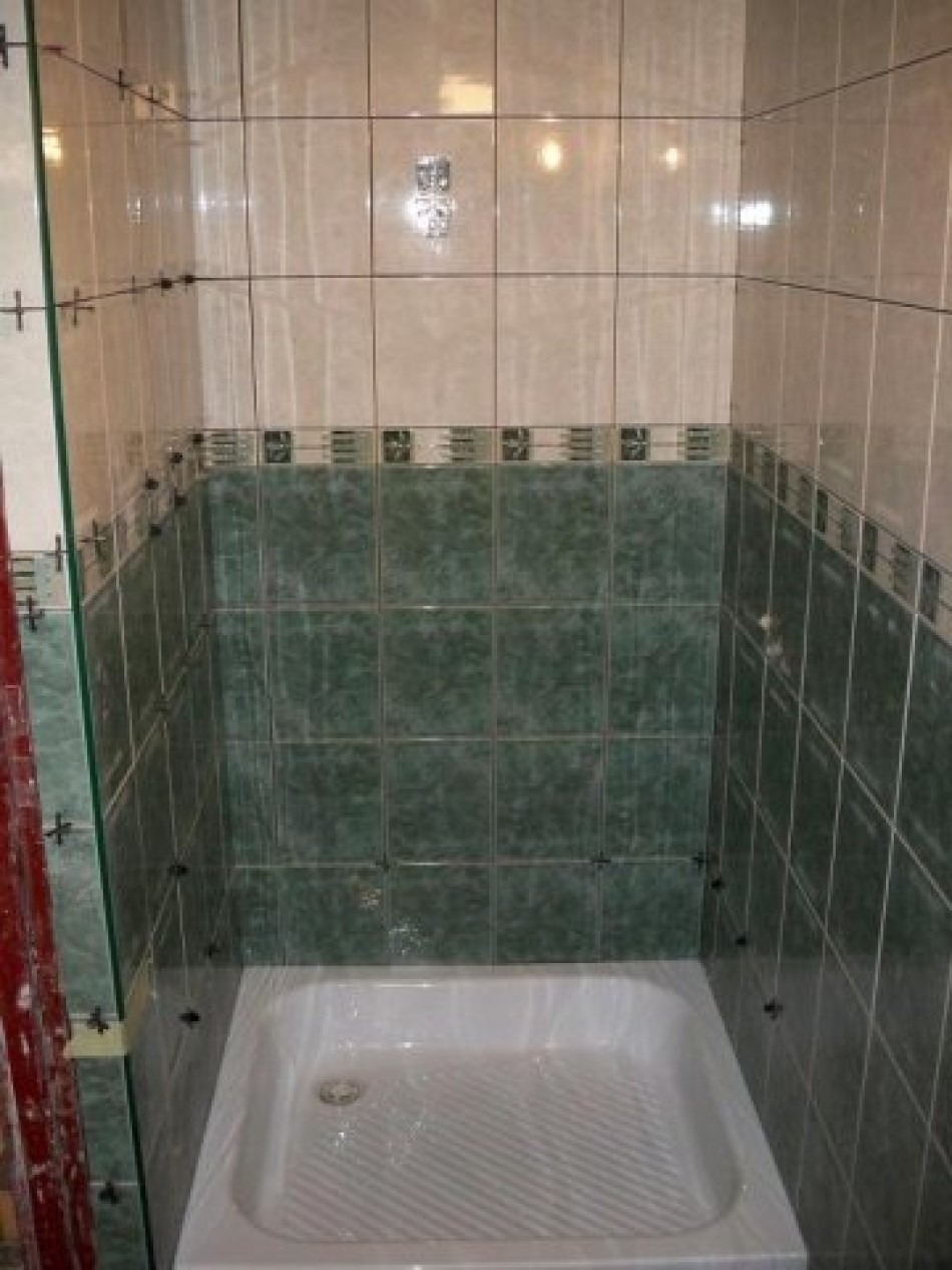 Montaż zielonych i kremowych płytek w kabinie prysznicowej, widoczne krzyżyki dystansowe, biały brodzik. W tle widoczna drabina malarska.