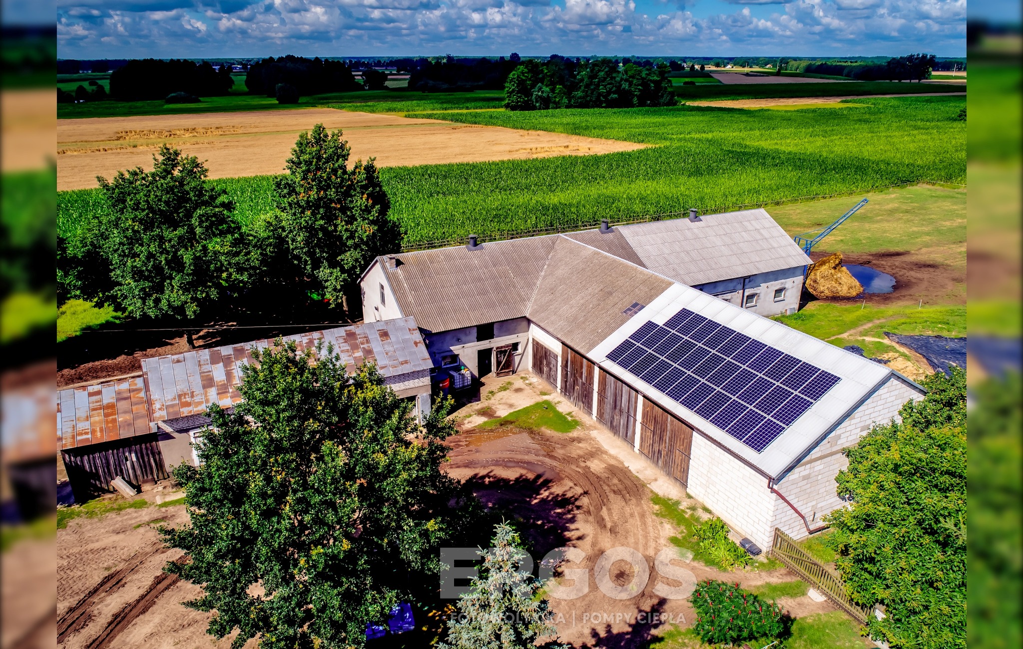 Widok z lotu ptaka na budynki gospodarcze z panelami słonecznymi na dachu w Brodnicy, otoczone polami uprawnymi i drzewami, z widocznymi śladami opon na dziedzińcu.