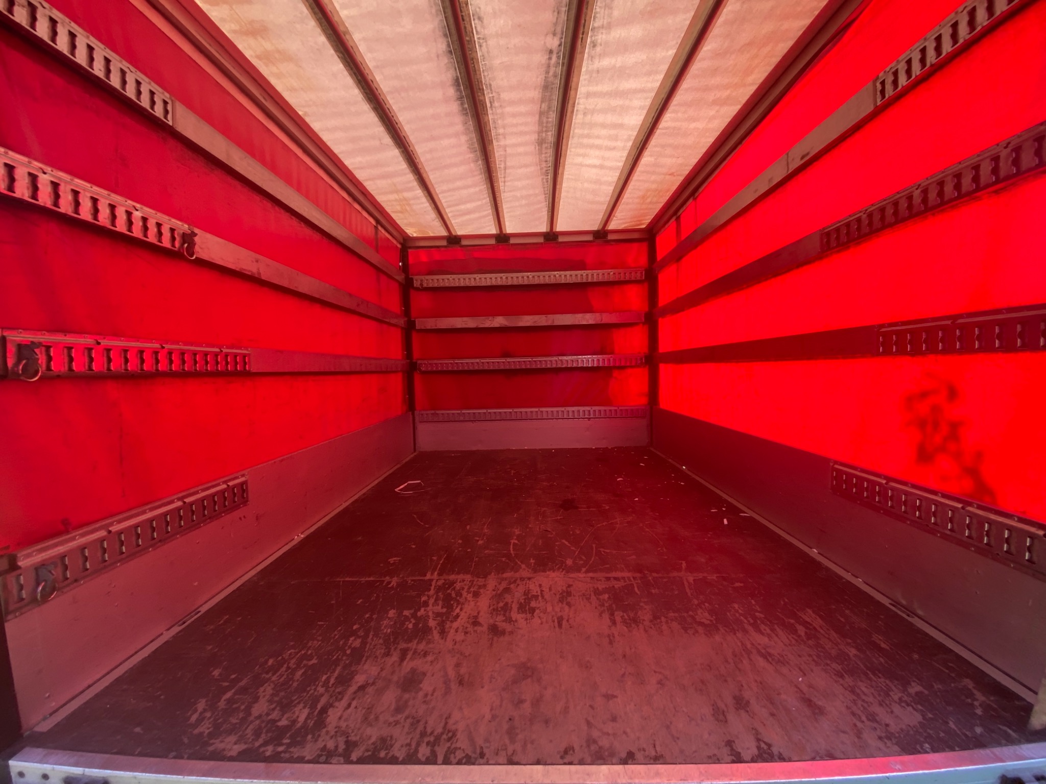 Wnętrze pustej, czerwonej furgonetki do przeprowadzek z mocowaniami ładunku na ścianach i suficie, widok z tyłu.