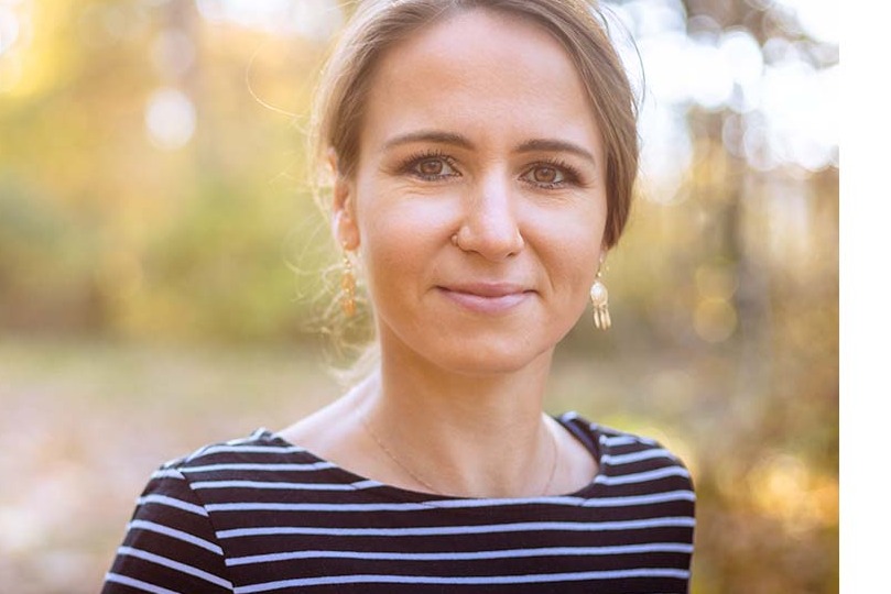 Portret kobiety z kolczykami w kształcie frędzli, w tle rozmyte drzewa w jesiennych barwach.