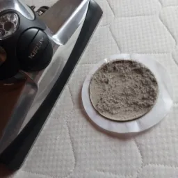 Fragment materaca po czyszczeniu odkurzaczem Kirby, obok próbka zebranego brudu na białym filtrze.