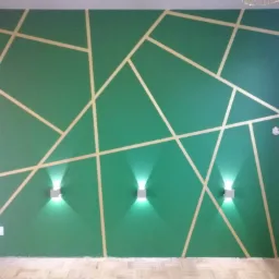 Szmaragdowa ściana z geometrycznym wzorem z jasnych pasków, oświetlona trzema nowoczesnymi kinkietami, widoczne gniazdka elektryczne i fragment parkietu.