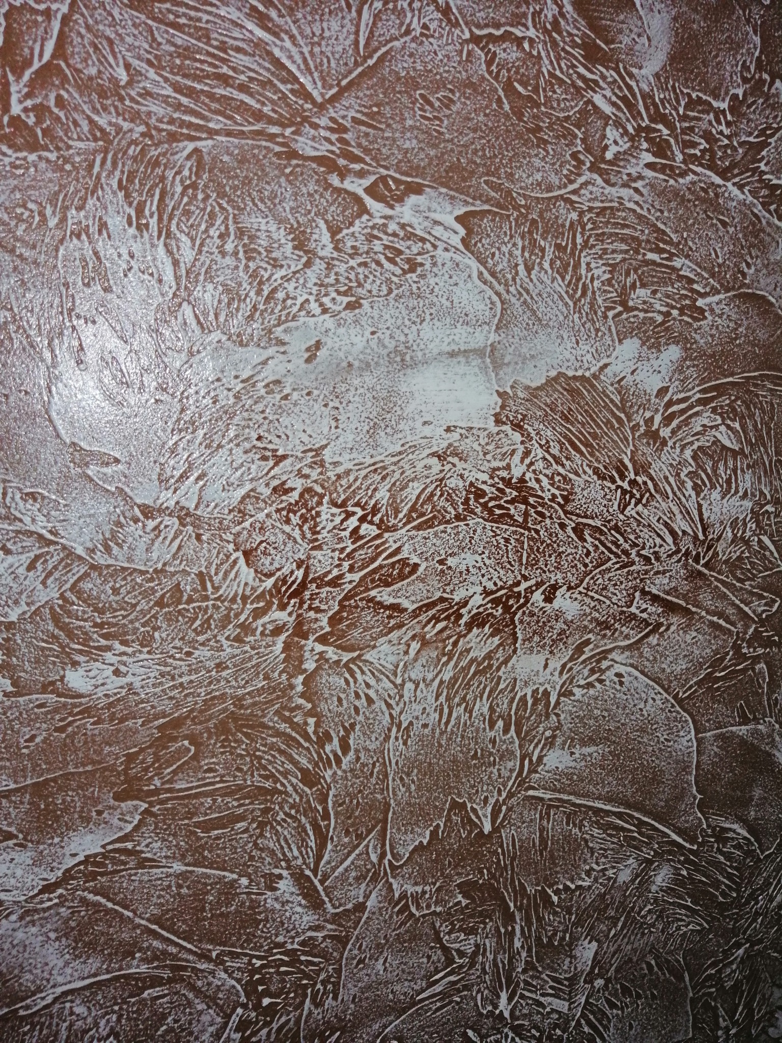 Brązowa ściana z dekoracyjną, nierównomierną fakturą w odcieniach bieli, przypominająca wzór mrozu na szybie.