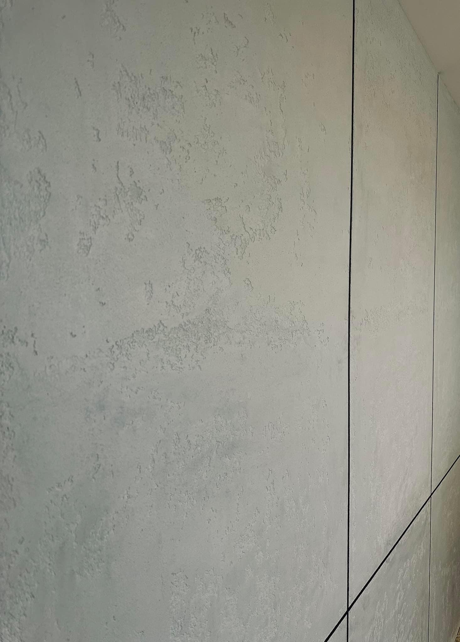 Szara ściana z dekoracyjną fakturą i czarnymi, pionowymi listwami wykończeniowymi, widok pod kątem.