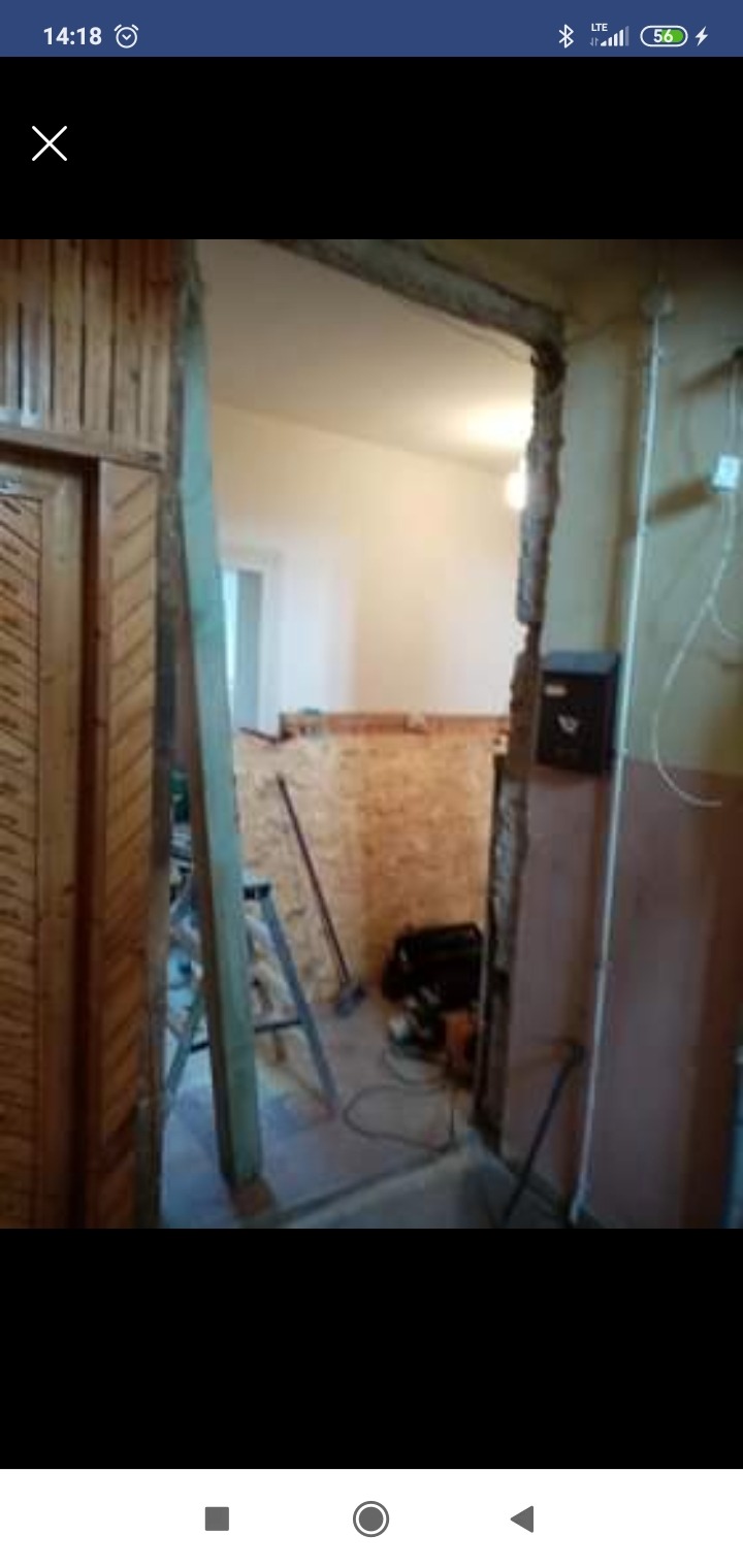 Demontaż ościeżnicy drzwiowej w trakcie remontu, widoczne uszkodzenia muru, drabina, narzędzia i płyta OSB.