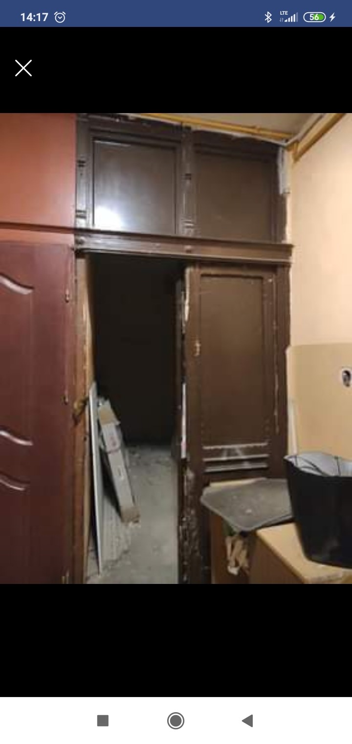 Demontaż starych, brązowych drzwi wewnętrznych z widocznymi uszkodzeniami i pozostałościami po farbie, z fragmentami ościeżnicy i widokiem na ciemne wnętrze pomieszczenia.