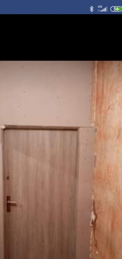 Drewniane drzwi wewnętrzne z klamką na tle ściany z odchodzącą farbą, widoczne ślady po remoncie.