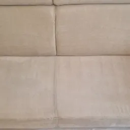 Jasnobeżowa kanapa z widocznymi śladami czyszczenia, pokazująca różnicę w odcieniu między wyczyszczoną a nieczyszczoną częścią, z delikatnym połyskiem na wyczyszczonej powierzchni.