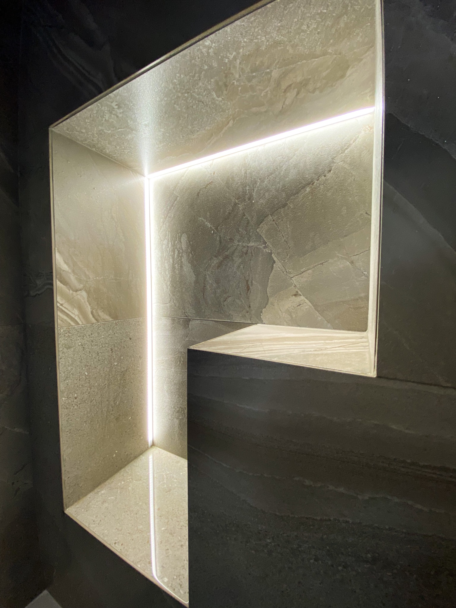 Wnęka w ścianie wyłożona beżowymi i szarymi płytkami z subtelnym oświetleniem LED, wykonana w Krakowie.