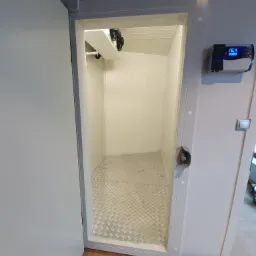 Wnętrze chłodni z ryflowaną podłogą, widoczny agregat chłodniczy i panel sterowania z wyświetlaczem temperatury.