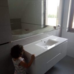 New home Krystian Ampulski - Nowoczesna łazienka z białymi płytkami, umywalką z szafką i dużym lustrem, widoczna mała dziewczynka w rogu.
