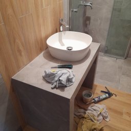 TOM-GRES - Montaż umywalki nablatowej w łazience z widocznymi narzędziami i materiałami budowlanymi na podłodze, obok kabina prysznicowa.