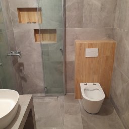 TOM-GRES - Nowoczesna łazienka z szarymi marmurkowymi płytkami, kabiną prysznicową ze szklanymi drzwiami, podwieszaną toaletą z drewnianą obudową i wnękami w ścianie obłożonymi drewnem; na podłodze leży...