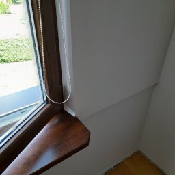 TOM-GRES - Drewniane okno z roletą koralikową w jasnym pokoju na poddaszu, widoczny fragment podłogi przed wykończeniem listwami przypodłogowymi.