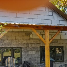 TOM-GRES - Zadaszenie tarasu z drewnianą konstrukcją w Obszy, ściany z szarego bloczka, widoczne okna i meble ogrodowe.