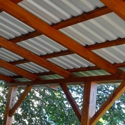 TOM-GRES - Drewniana konstrukcja z metalowym dachem, widok z dołu, z widocznymi drzewami w tle.