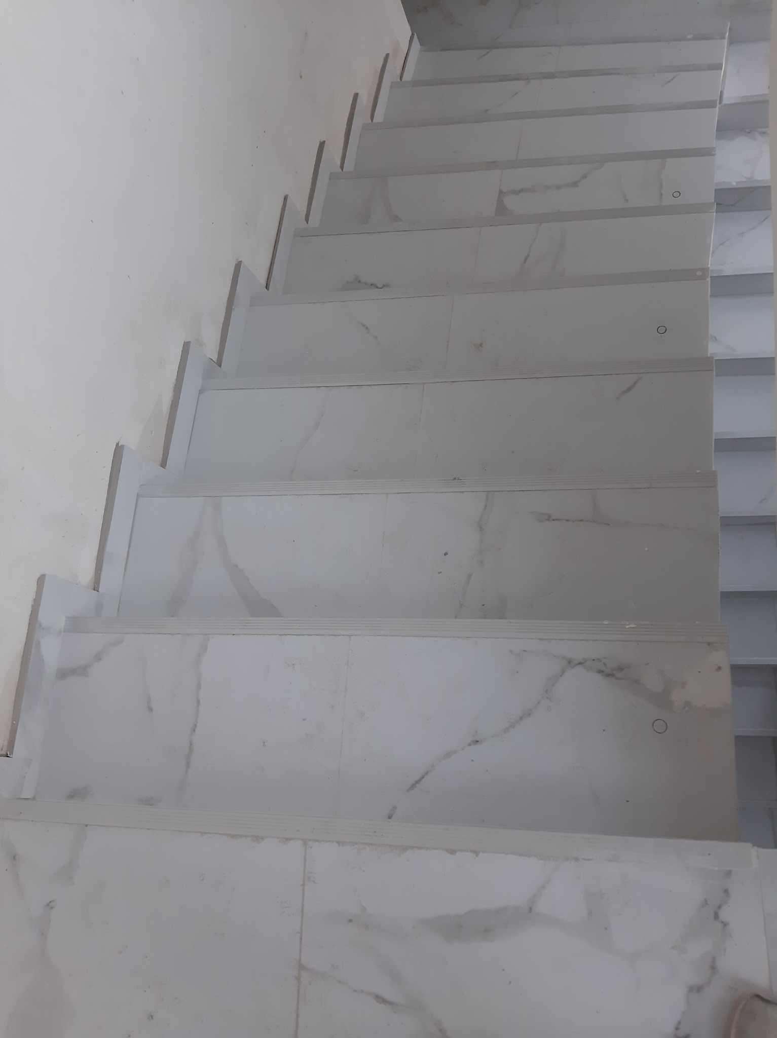Schody wyłożone białymi płytkami imitującymi marmur, widok z góry, z delikatnym oświetleniem podkreślającym wzór płytek.