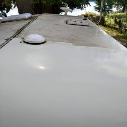 PureSteam - mobilna myjnia parowa - Częściowo umyta, płaska powierzchnia dachu z elementami wyposażenia, widoczne ślady brudu i zacieków, w tle drzewa i jezioro.