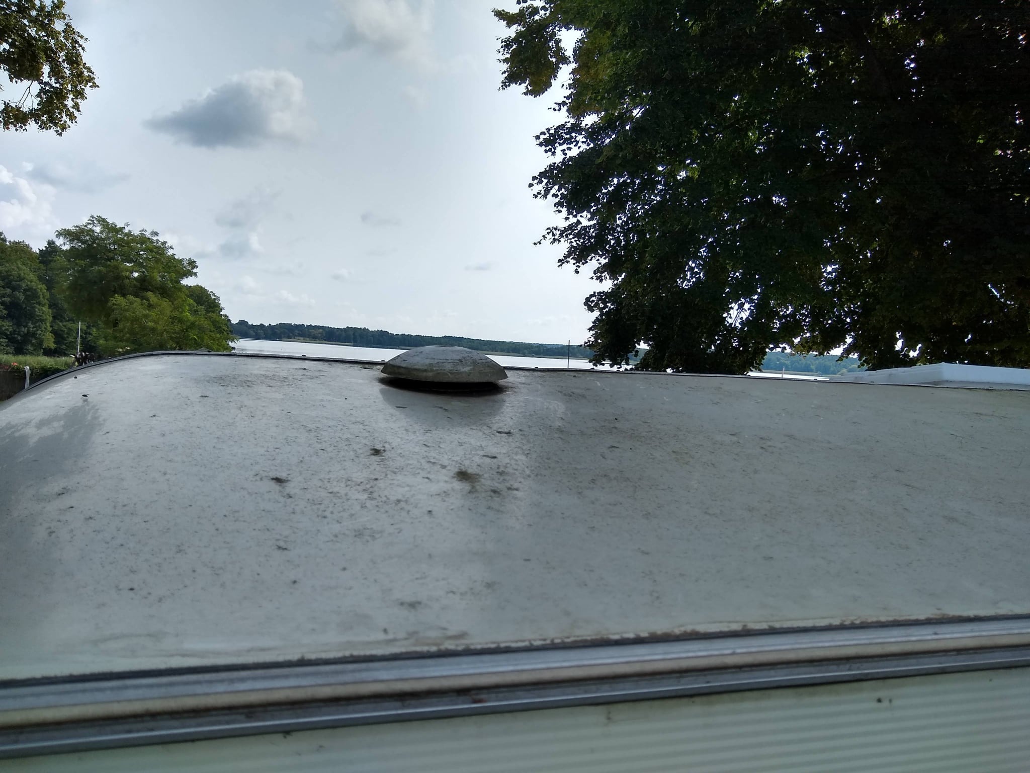 Brudny dach przyczepy kempingowej z widocznym jeziorem i drzewami w tle, wymagający umycia.