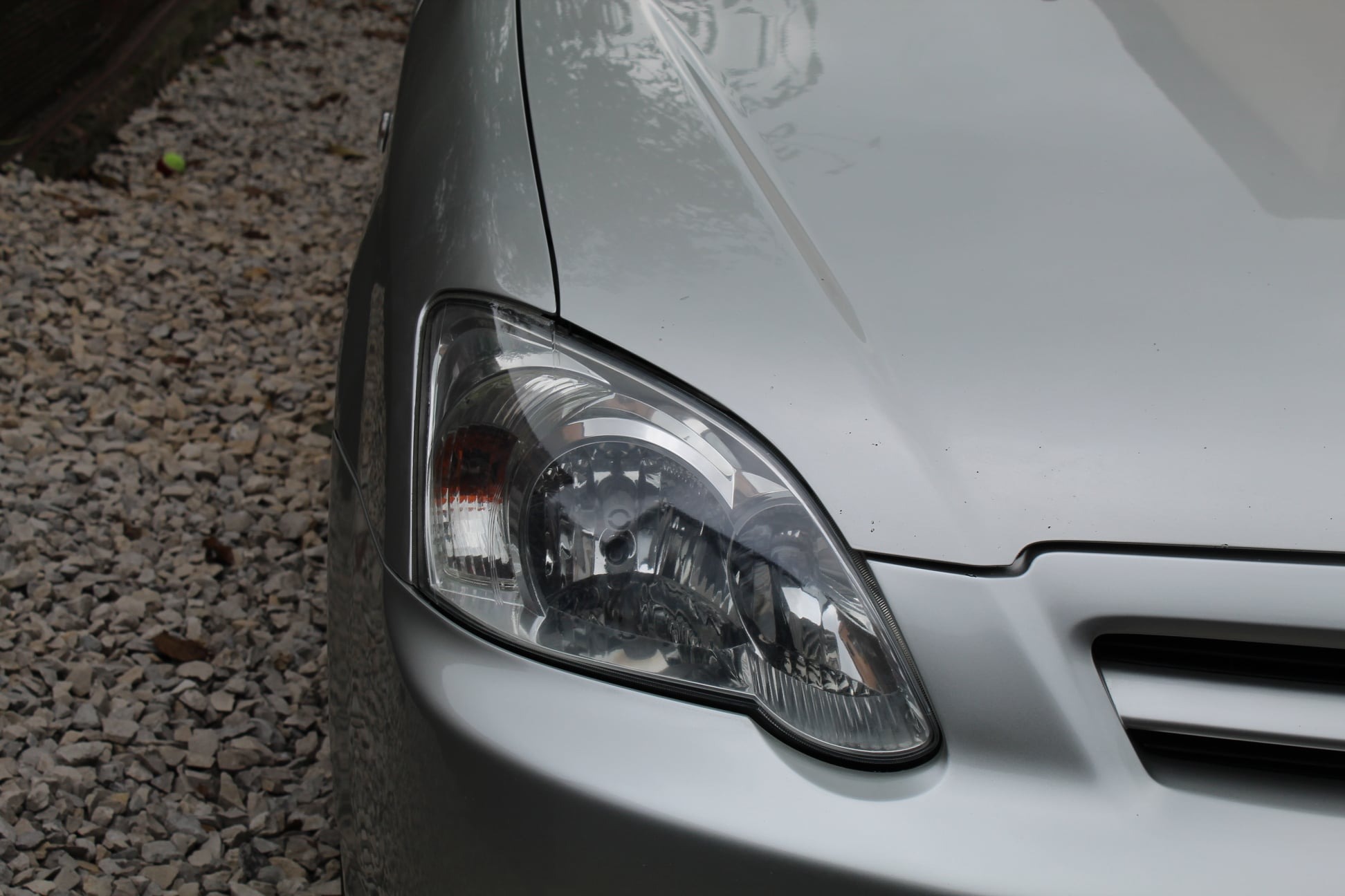 Srebrny samochód, widok na przedni reflektor i fragment karoserii, tło z szarych kamieni