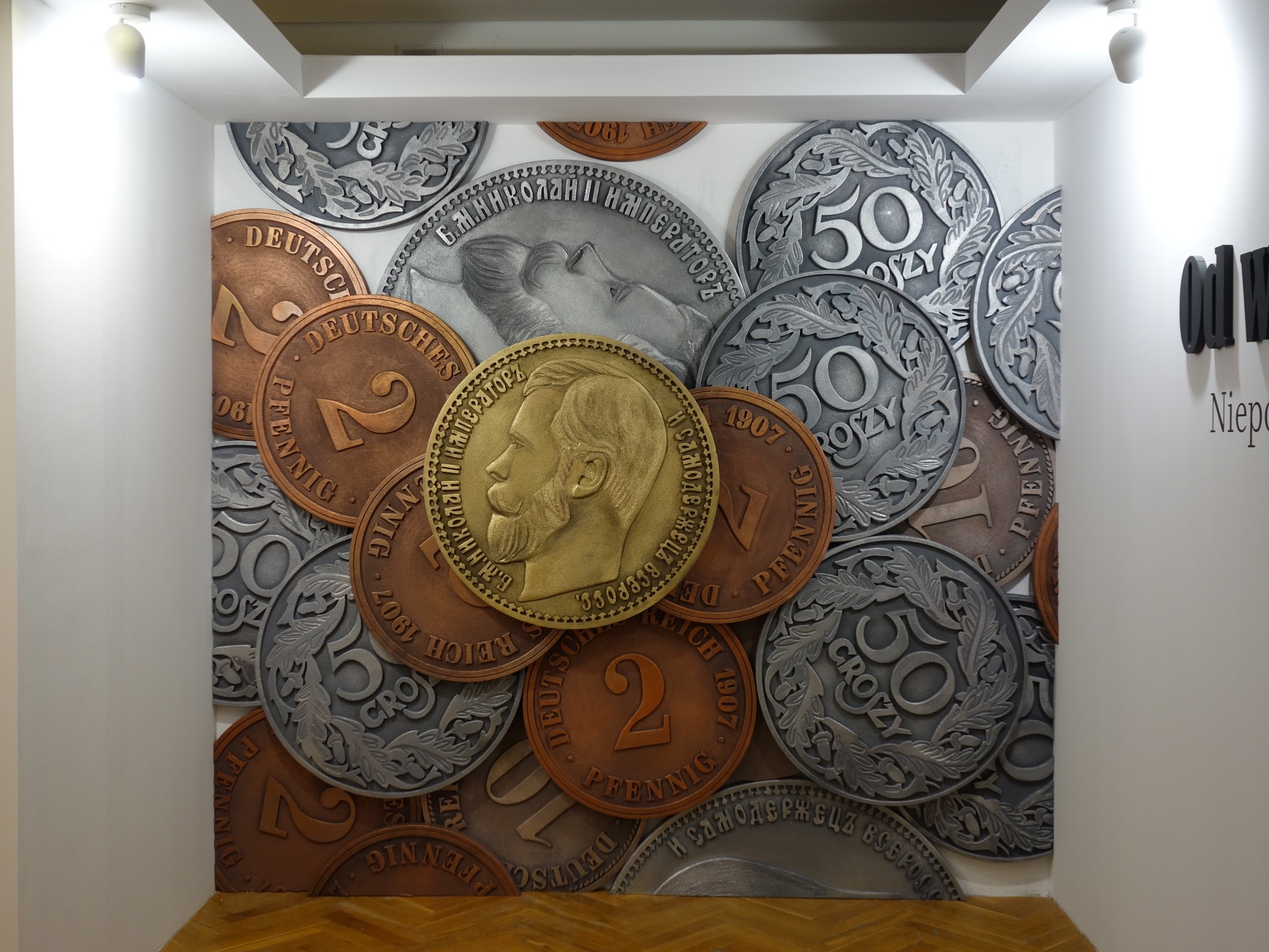 Dekoracyjna ściana z dużych, stylizowanych monet w odcieniach złota, srebra i brązu, tworzących trójwymiarową kompozycję.