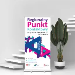 Roll-up reklamowy Regionalnego Punktu Kontaktowego Programów Ramowych UE w Szczecinie, z widocznymi danymi kontaktowymi i logotypami, ustawiony w minimalistycznym wnętrzu obok dekoracyjnej rośliny...