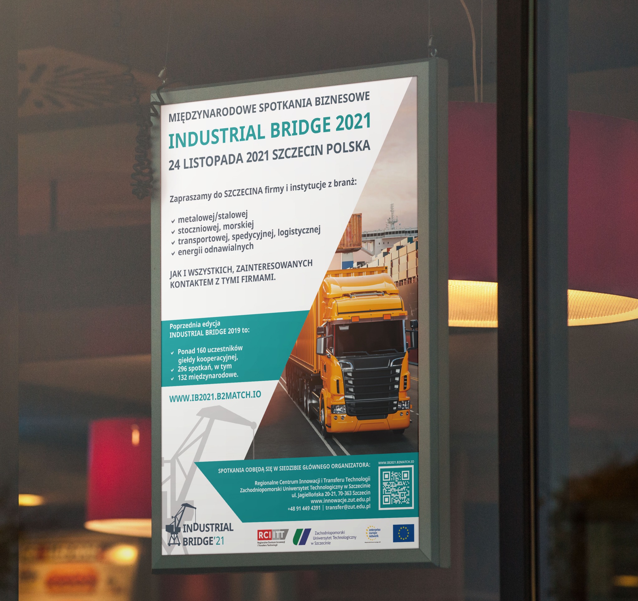 Plakat reklamowy Międzynarodowych Spotkań Biznesowych Industrial Bridge 2021, z ilustracją żółtej ciężarówki na tle portu, zawieszony w oknie z widocznym odbiciem wnętrza budynku.