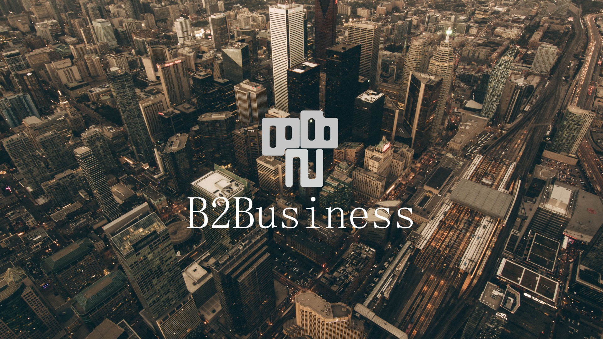 Widok z lotu ptaka na gęsto zabudowane miasto z wieżowcami, torami kolejowymi i autostradą, z nałożonym logo i tekstem 'B2Business'.
