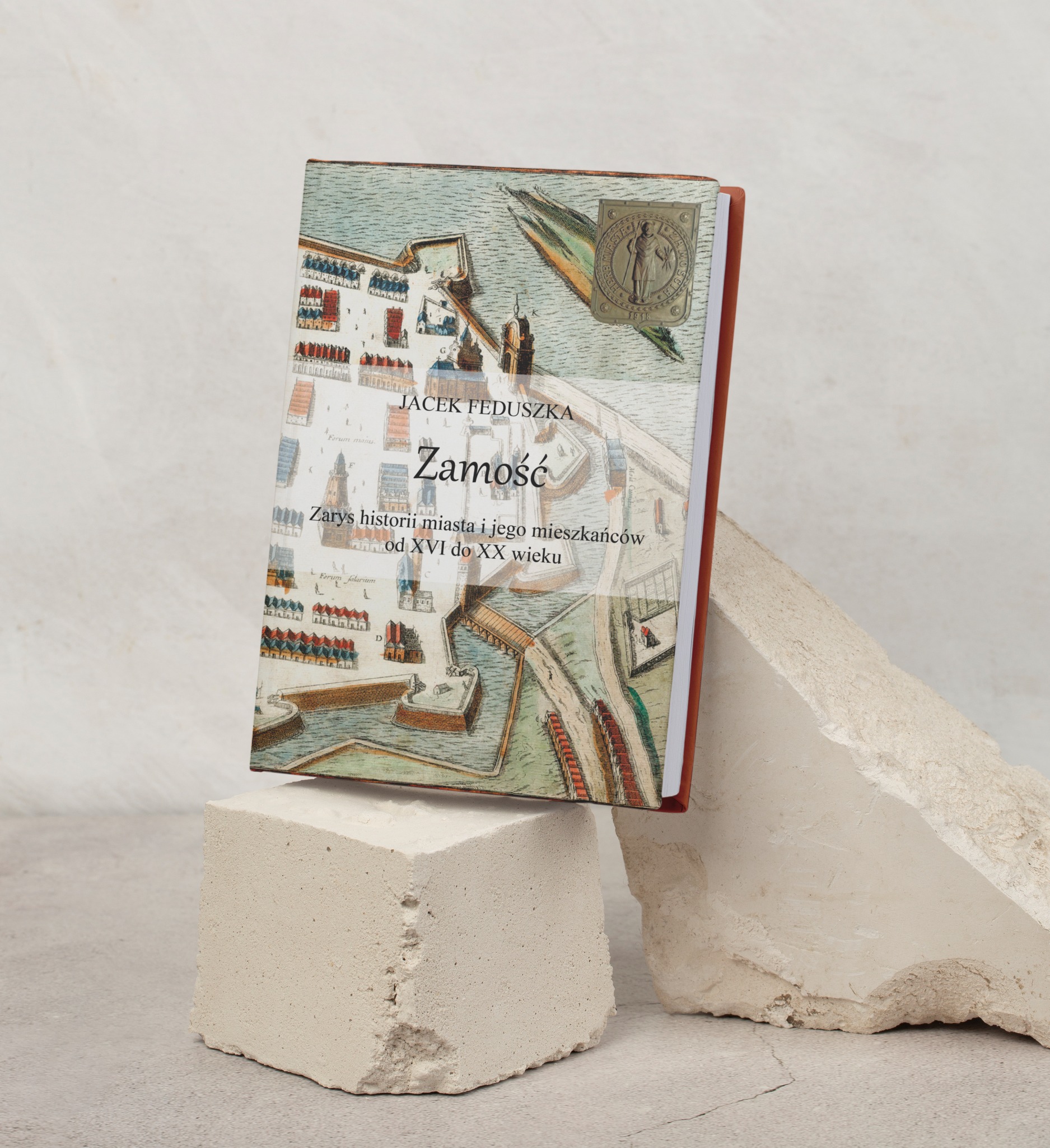 Książka o Zamościu autorstwa Jacka Feduszki z planem miasta na okładce, umieszczona na betonowym bloku.