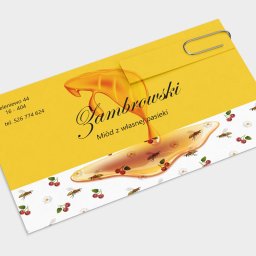 Neko Card - Żółta wizytówka z motywem miodu, wisien i pszczół, spięta srebrnym spinaczem biurowym. Wizytówka prezentuje nazwę firmy 'Zambrowski' oraz dopisek 'Miód z własnej pasieki', a także dane kontaktowe.