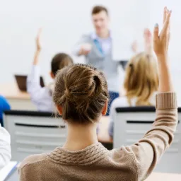 Uczestnicy podnoszą ręce podczas wykładu, prowadzący prezentuje dokument, widok zza pleców uczestników.