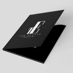 Czarna, otwarta teczka firmowa z logo 'The Estate Warsaw' w białym kolorze, leżąca na jasnym tle.