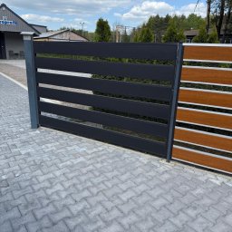 DaMet Damian Napora - Nowoczesne ogrodzenie panelowe z poziomymi, czarnymi przęsłami i drewnopodobnymi elementami, widoczne na tle kostki brukowej i zieleni. Minimalistyczny design.